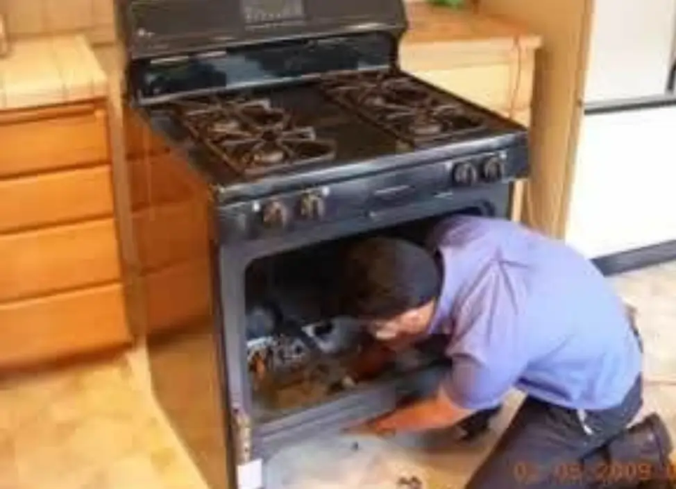 Technician kneeling on the floor repairing a Cooking Range with an oven in a home kitchen.